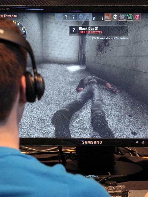 Ein junger Mann sitzt am Bildschirm und spielt. Auf dem Monitor ist die Abbildung einer getöteten Person zu sehen und zu lesen, dass der User sie getötet hat.