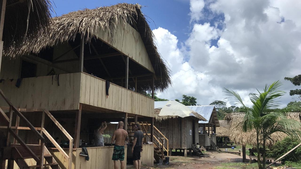 Ein einfaches Holzhaus mit einer Treppe, davor stehen zwei Männer Ein einfaches Holzhaus mit einer Treppe, davor stehen zwei Männer