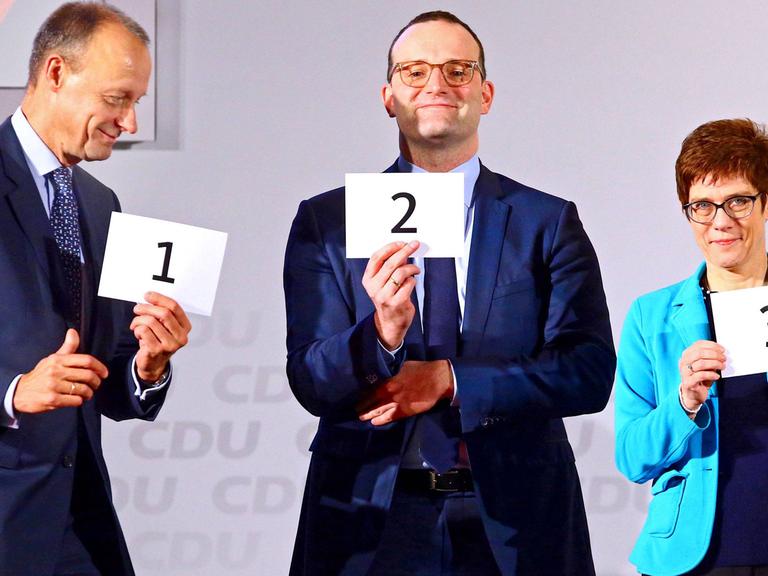 Friedrich Merz, Jens Spahn und Annegret Kramp Karrenbauer halten Zettel mit Zahlen in die Höhe.