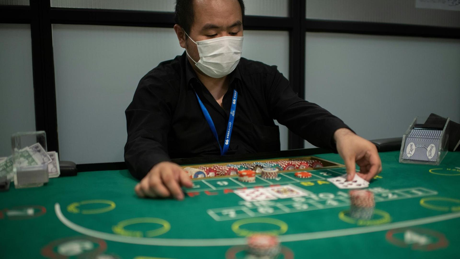 Ein angehender Croupier und Student der Japan Casino School in Tokio spielt mit Mundschutz das Karten-Glücksspiel Baccarat Ein angehender Croupier und Student der Japan Casino School in Tokio spielt mit Mundschutz das Karten-Glücksspiel Baccarat