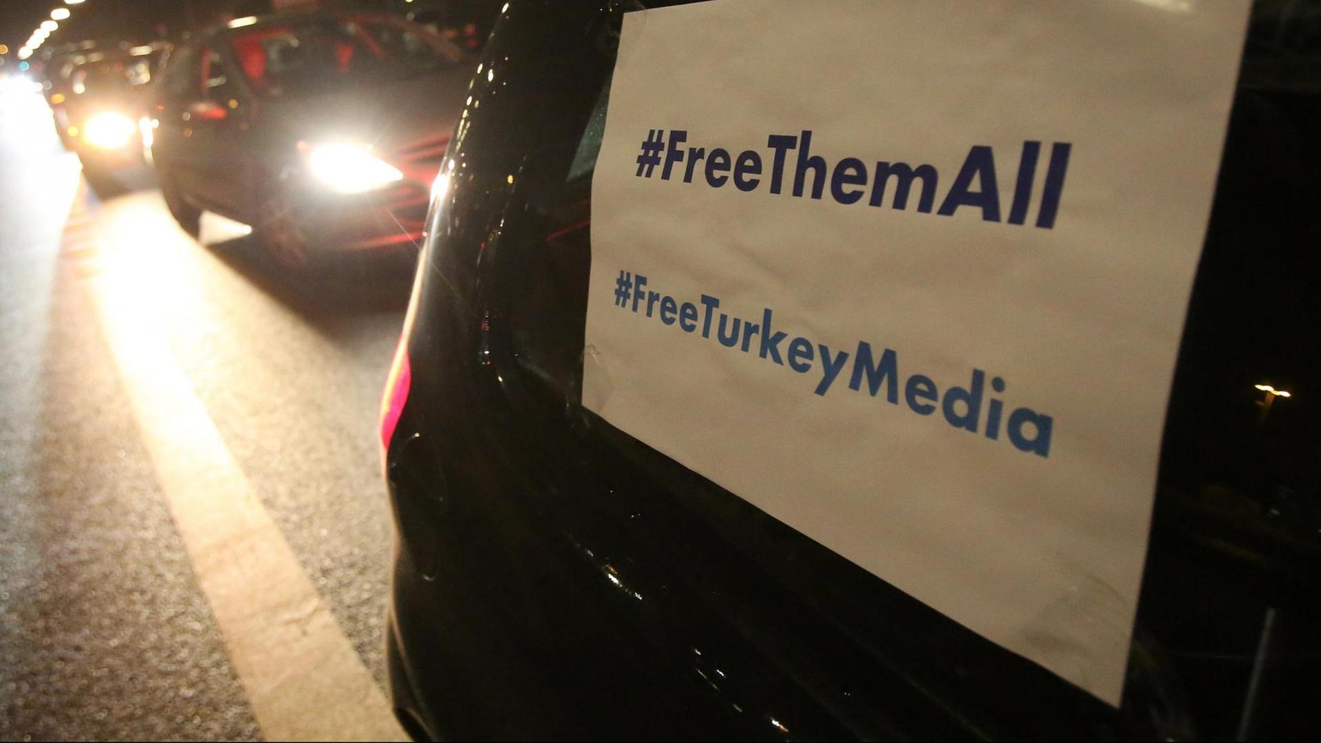 In einem Auto ist ein Plakat mit der Aufschrift "#FreeThemAll" und "FreeTurkeyMedia" an einem Auto zu sehen.