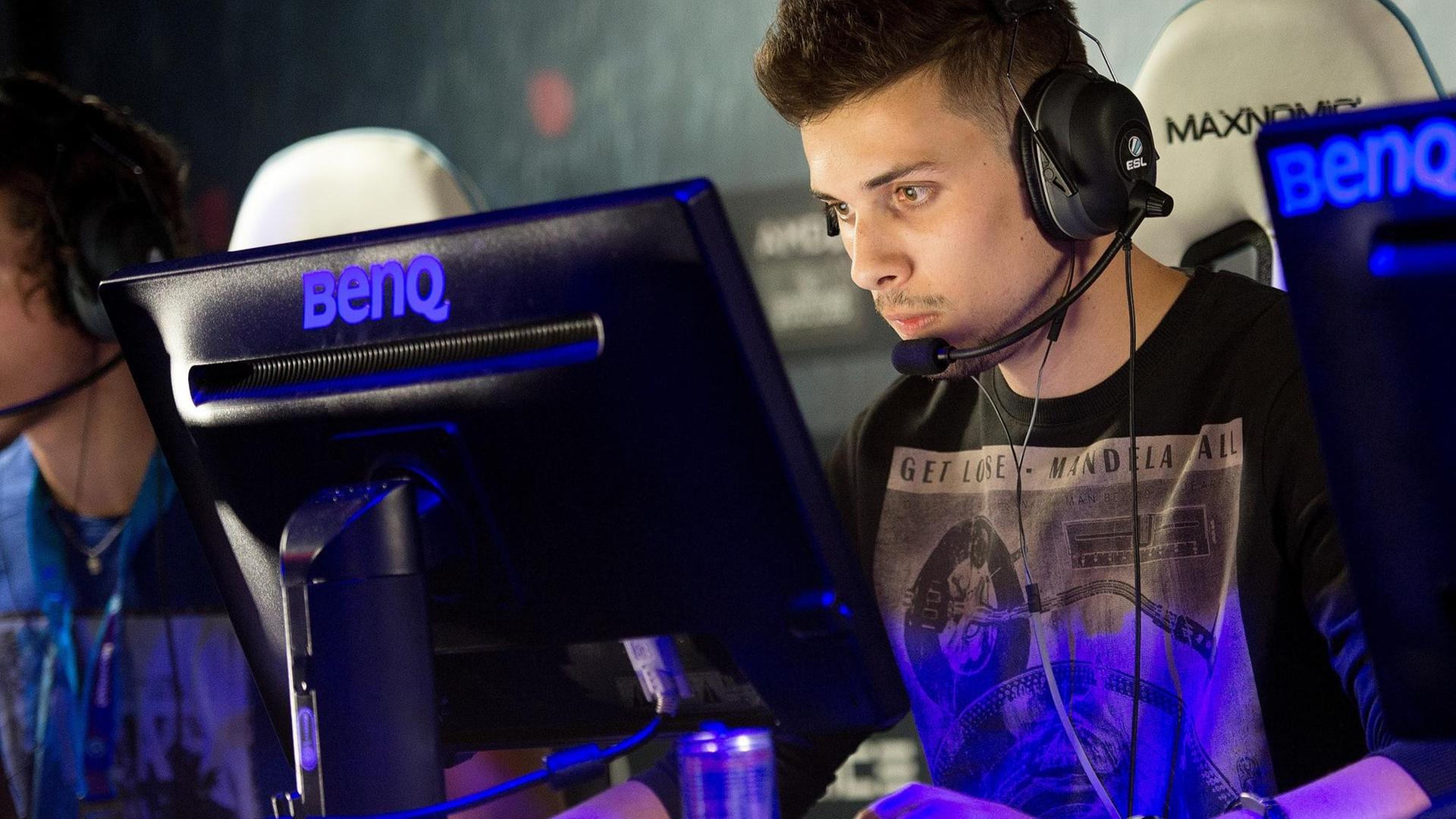 Ein Spieler sitzt mit Kopfhörer und Mikrofon vor einem Monitor. Ein Spieler sitzt mit Kopfhörer und Mikrofon vor einem Monitor.