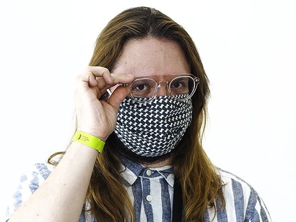 Portrait des Autors Micha Kranixfeld vor einem weißen Hintergrund; Mund und Nase hat er mit einer Maske geschützt; aus seiner Umhängetasche, die er vor dem Oberkörper zu hängen hat, kuckt eine Desinfektionssprühflasche heraus; mit der Hand fasst er sich rechts an seine Brille Portrait des Autors Micha Kranixfeld vor einem weißen Hintergrund; Mund und Nase hat er mit einer Maske geschützt; aus seiner Umhängetasche, die er vor dem Oberkörper zu hängen hat, kuckt eine Desinfektionssprühflasche heraus; mit der Hand fasst er sich rechts an seine Brille