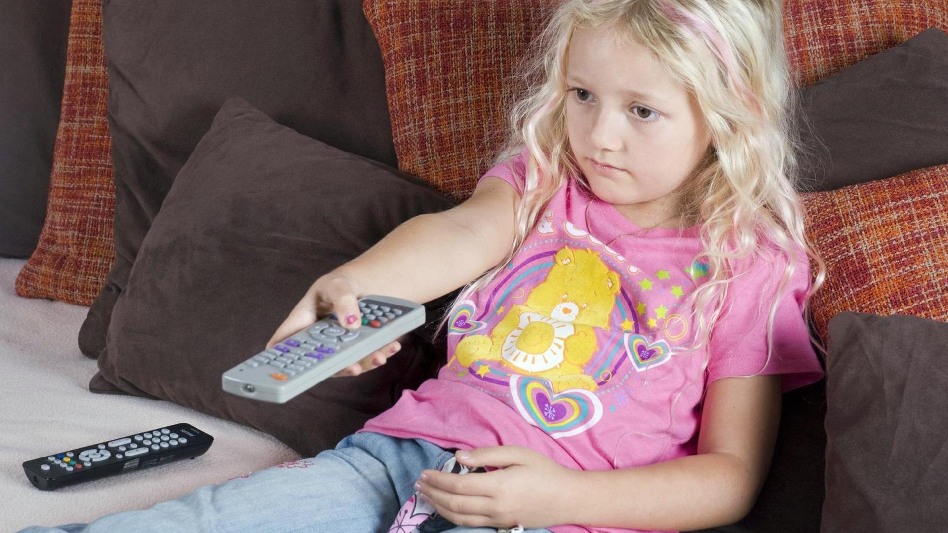 Ein Mädchen sitzt auf der Couch und hält eine Fernbedienung in der Hand Ein Mädchen sitzt auf der Couch und hält eine Fernbedienung in der Hand