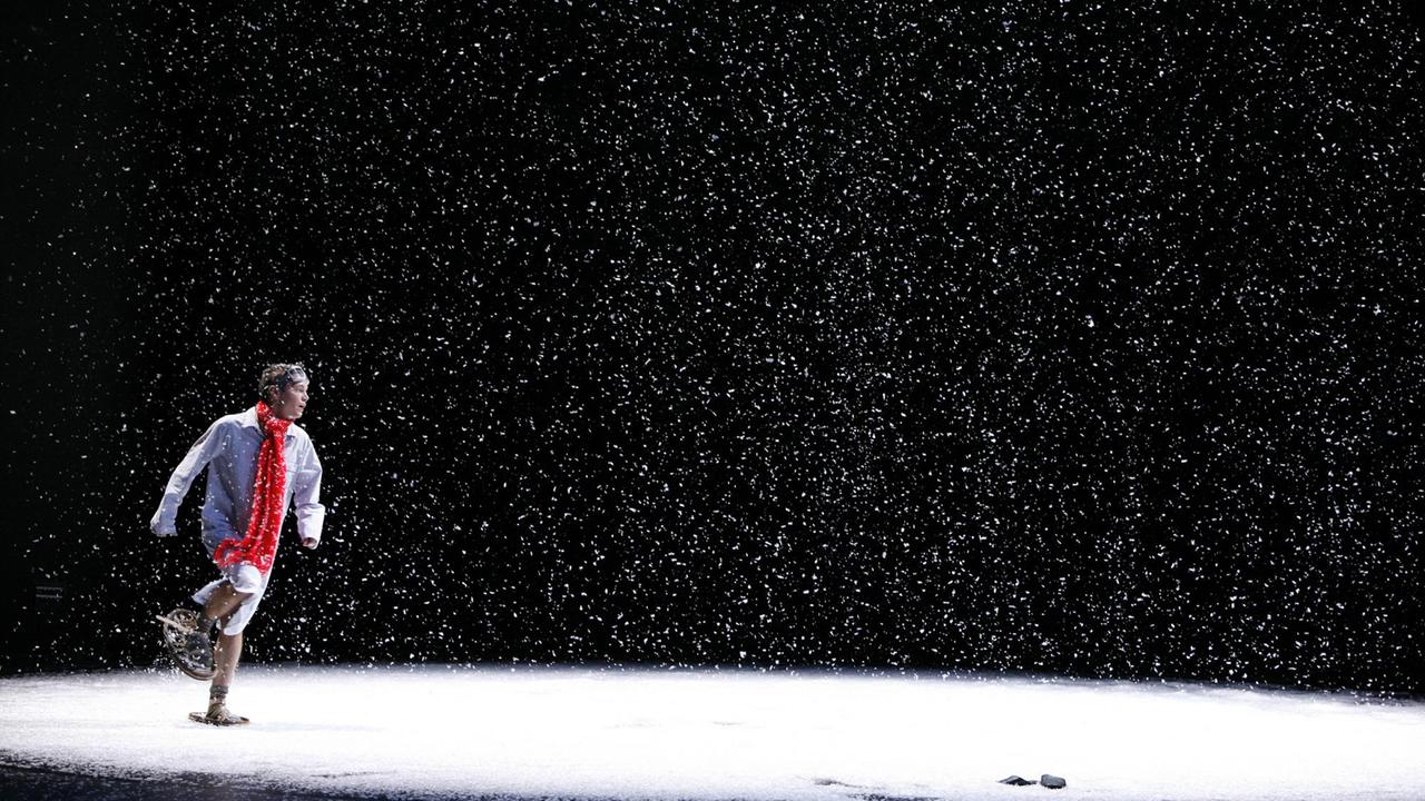 Eine schneebedeckte Bühne auf der eine Person mit rotem Schal und Schneeschuhen zu sehen ist. Eine schneebedeckte Bühne auf der eine Person mit rotem Schal und Schneeschuhen zu sehen ist.