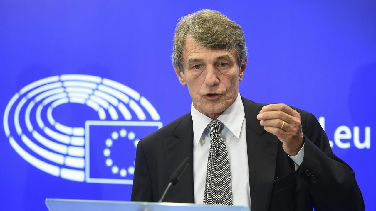 Sassoli steht vor einer blauen Wand mit dem Logo des EU-Parlaments und spricht in ein Mikrofon.