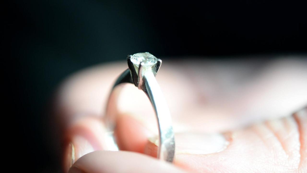 Eine Hand hält einen schmalen Ring mit einem eingefassten Diamanten Eine Hand hält einen schmalen Ring mit einem eingefassten Diamanten