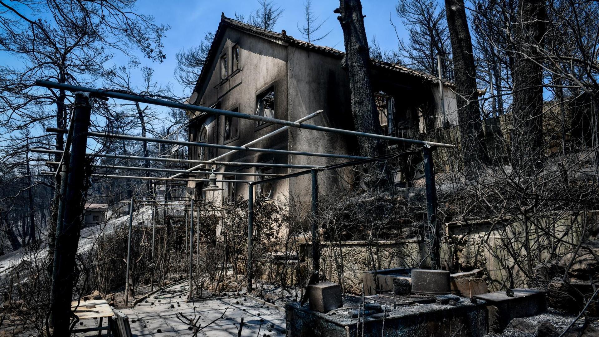 Das Foto zeigt ein abgebranntes Haus und weitere Feuerschäden nach den verheerenden Waldbränden in Griechenland.