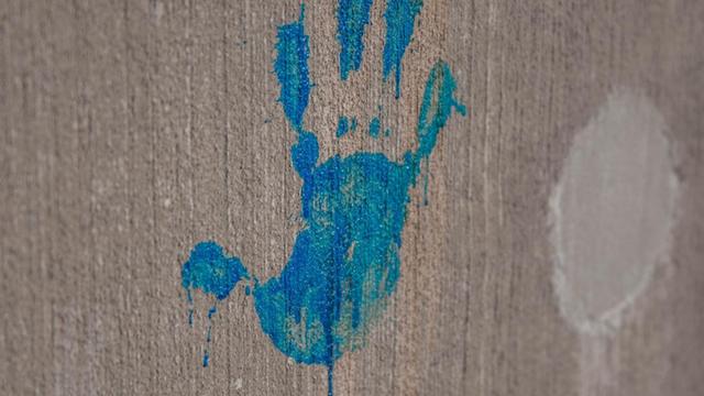 Handabdruck aus blauer Farbe an einer grauen Wand