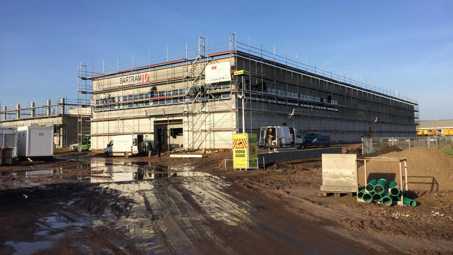 Ein Baustelle in Neumünster: Von einem Baugerüst umgeben steht eine kastenförmige Halle Ein Baustelle in Neumünster: Von einem Baugerüst umgeben steht eine kastenförmige Halle