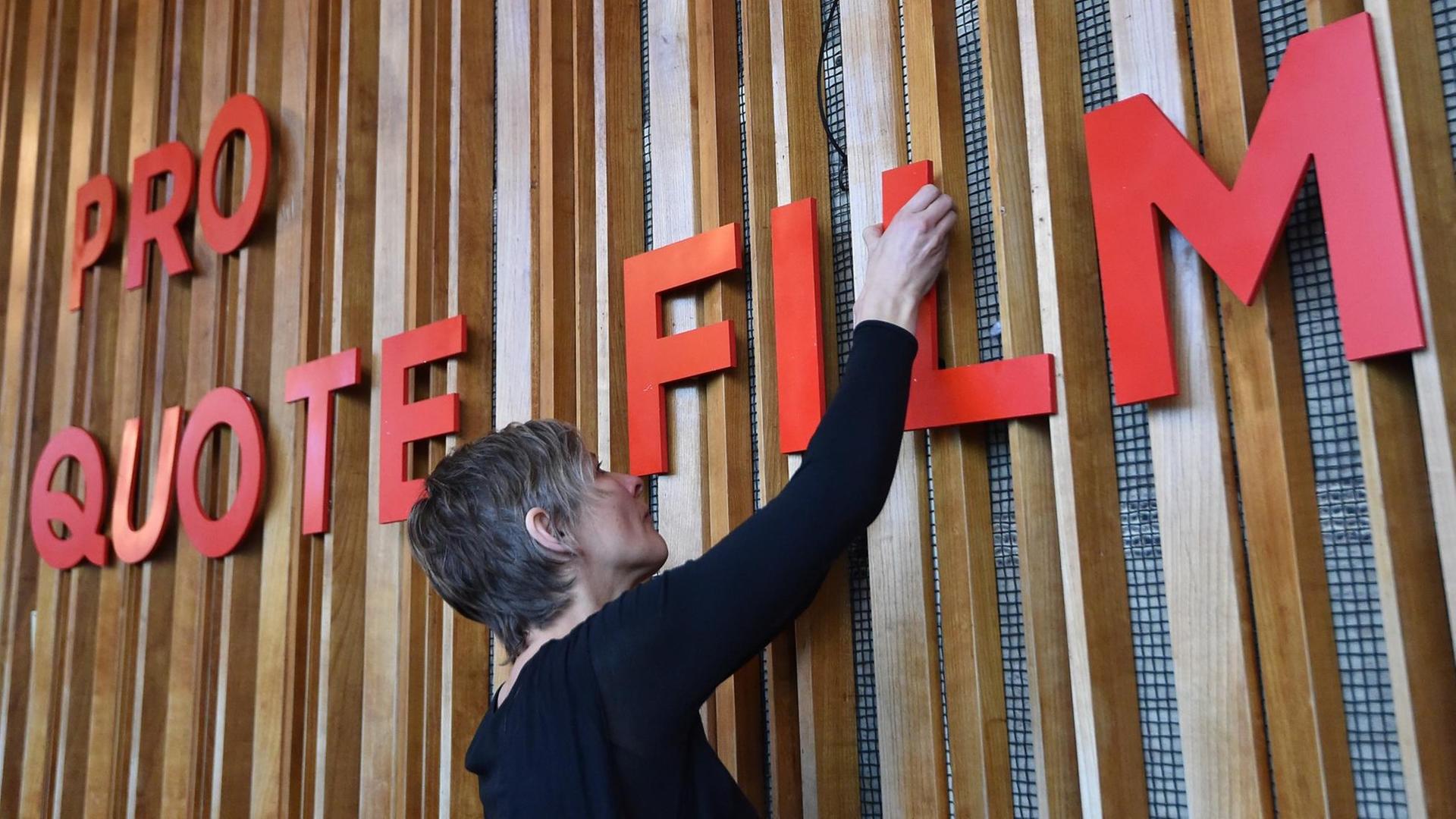31.01.2018, Berlin: Ein Frau bringt im Kino Kosmos den Slogan "Pro Quote Film" an. Der neue Zusammenschluss von Frauen aus allen Gewerken der Filmbranche erweitert die bisherige Arbeit des Zusammenschlusses von Regisseurinnen auf die Gleichstellung von Frauen in allen Bereichen des Films. Foto: Bernd Settnik/dpa-Zentralbild/dpa | Verwendung weltweit 31.01.2018, Berlin: Ein Frau bringt im Kino Kosmos den Slogan "Pro Quote Film" an. Der neue Zusammenschluss von Frauen aus allen Gewerken der Filmbranche erweitert die bisherige Arbeit des Zusammenschlusses von Regisseurinnen auf die Gleichstellung von Frauen in allen Bereichen des Films. Foto: Bernd Settnik/dpa-Zentralbild/dpa | Verwendung weltweit