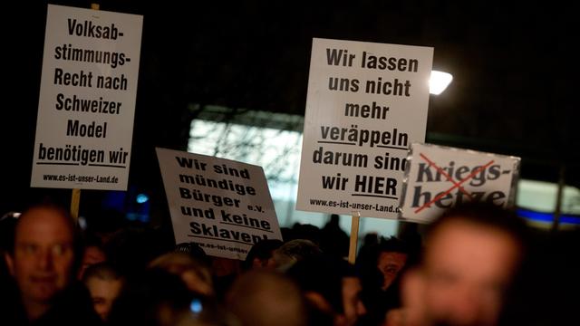 Teilnehmer einer Pegida-Kundgebung mit Plakaten in Dresden