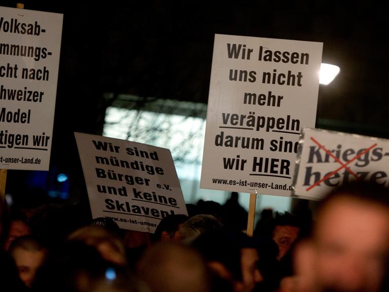Teilnehmer einer Pegida-Kundgebung mit Plakaten in Dresden