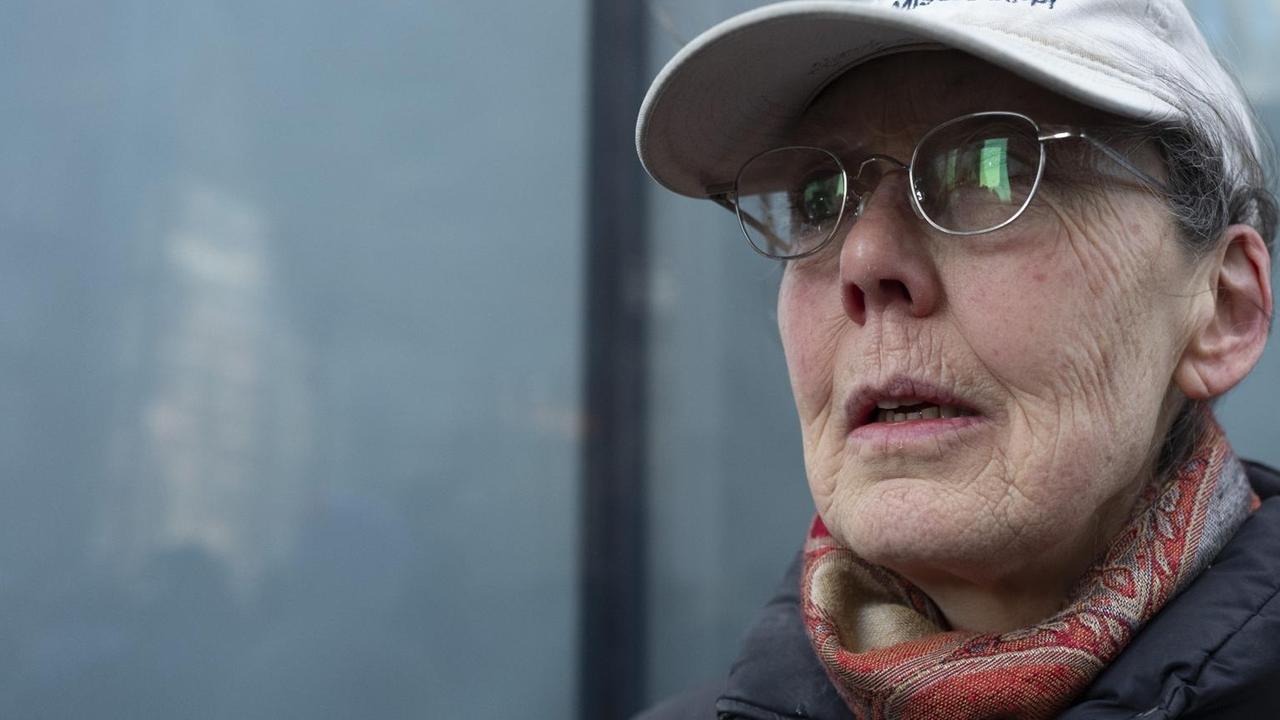 Die Schriftstellerin trägt ein Basecap und eine Brille und steht vor einer Glasfassade Die Schriftstellerin trägt ein Basecap und eine Brille und steht vor einer Glasfassade