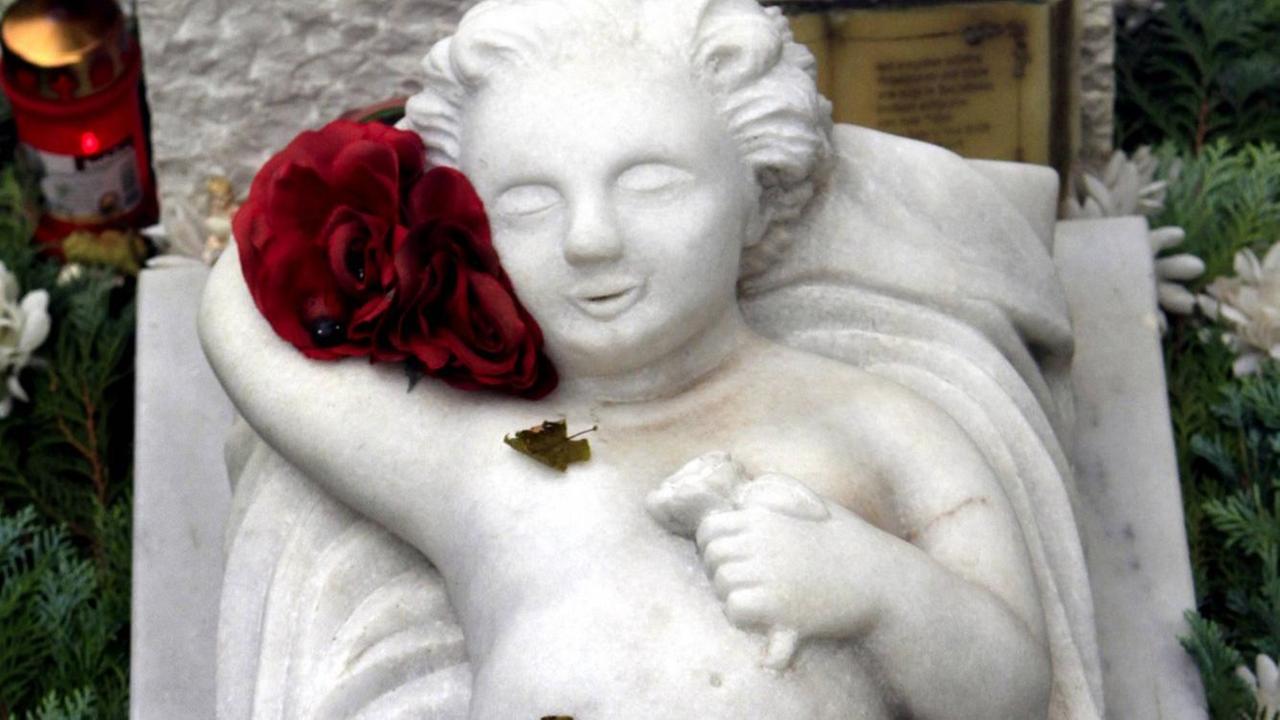 Grabplatte auf einem Kindergrab mit marmorner Engelsfigur auf einem Friedhof.