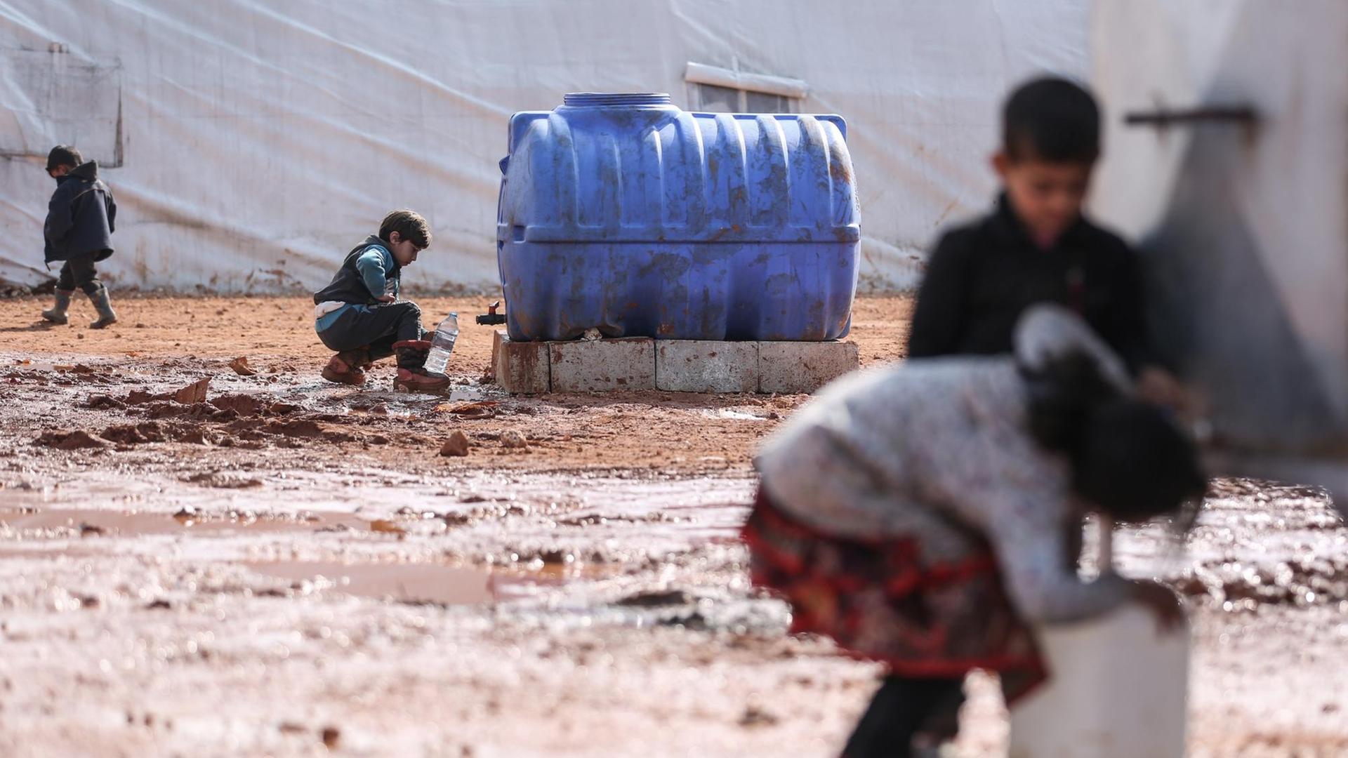 Syrische Kinder füllen in einem provisorischen Lager für Familien, die infolge der Bombardierung und der Militäroperationen aus dem Idlib-Land vertrieben wurden, Krüge mit Wasser auf.