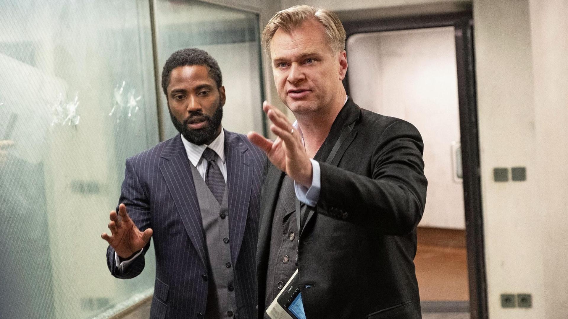 Christopher Nolan John David Washington stehen in einem engen Raum vor einer Scheibe mit Einschusslöchern. Nolan gibt Regieanweisungen. Christopher Nolan John David Washington stehen in einem engen Raum vor einer Scheibe mit Einschusslöchern. Nolan gibt Regieanweisungen.