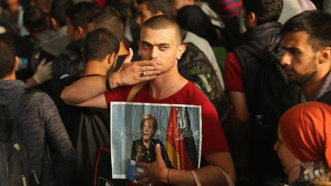 Ein vermutlich aus Syrien stammender Flüchtling macht eine Kusshand und hält dabei ein Bild von Angela Merkel in die Kamera, während er und etwa 800 weitere Personen aus Ungarn am 5. September 2015 am Münchner Hauptbahnhof in München eintreffen.