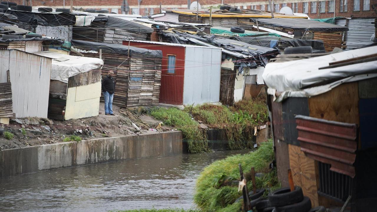 Ein Mann steht am Ufer eines Kanals, der durch den Township von Langa, Südafrika führt. Ein Mann steht am Ufer eines Kanals, der durch den Township von Langa, Südafrika führt.