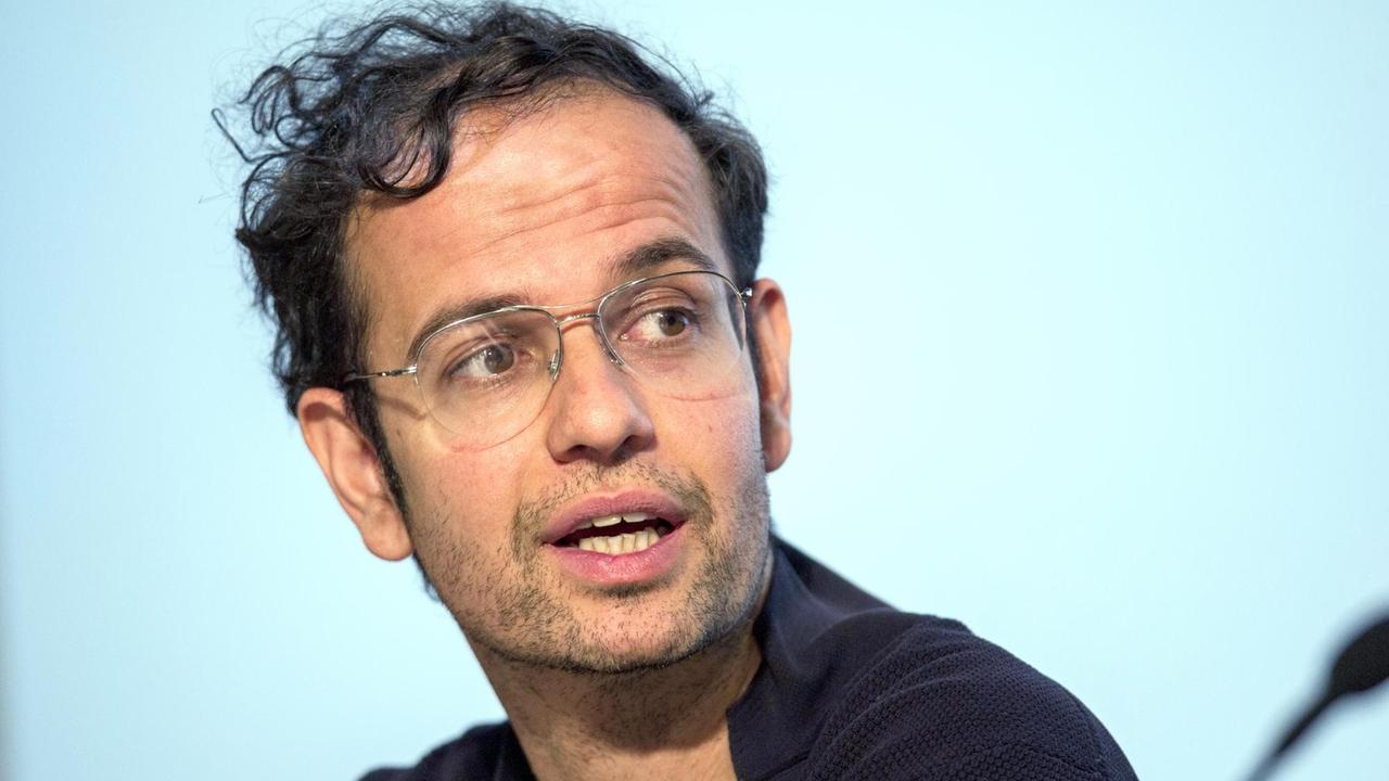Der Künstler Tino Sehgal sitzt bei einem Pressegespräch im Gropius-Bau vor einer angestrahlten Leinwand und stellt Pressevertretern seine Ausstellung vor Der Künstler Tino Sehgal sitzt bei einem Pressegespräch im Gropius-Bau vor einer angestrahlten Leinwand und stellt Pressevertretern seine Ausstellung vor