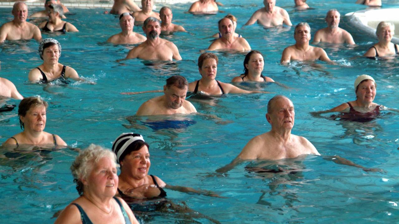 Auf dem vom Beckenrand Foto aufgenommenen Foto sind rund 20 Menschen zu sehen, die im Wasser eine medizinische Therapiestunde absolvieren.