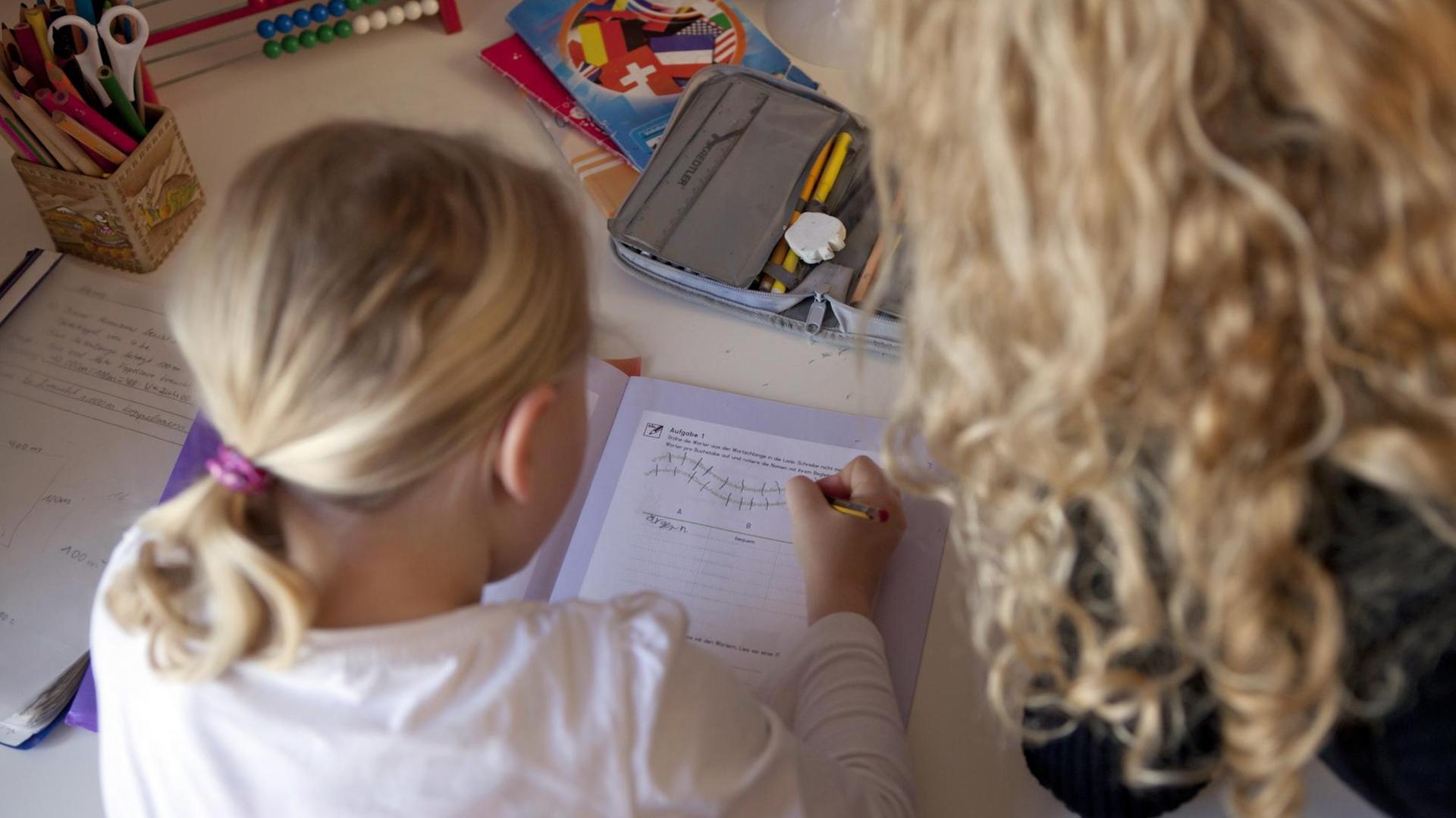 Das Bild zeigt eine Mutter, die ihrer Tochter über die Schulter guckt und bei Schulaufgaben hilft. Das Bild zeigt eine Mutter, die ihrer Tochter über die Schulter guckt und bei Schulaufgaben hilft.