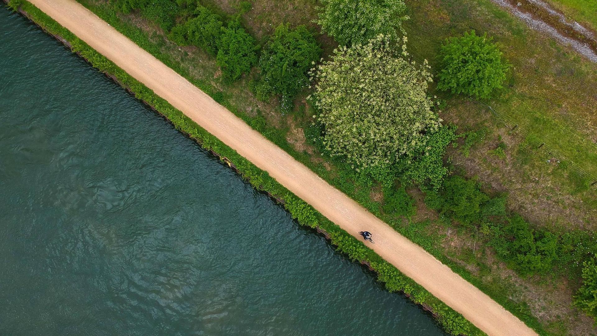 Luftaufnahme von der Emscher und einem Fahrradfahrer, der am Ufer entlang radelt.