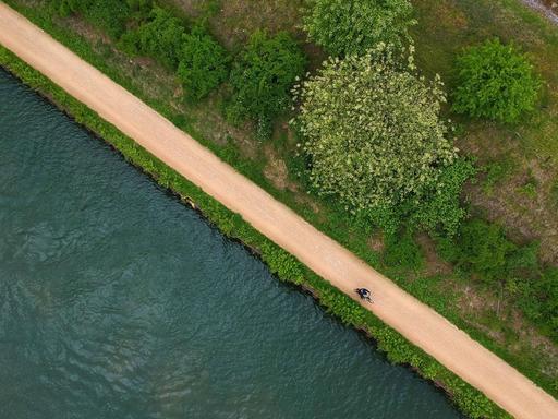 Luftaufnahme von der Emscher und einem Fahrradfahrer, der am Ufer entlang radelt.