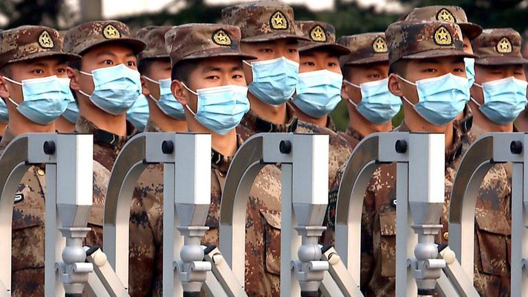 Chinesische Soldaten mit OP-Masken maschieren hinter einem Zaun. Chinesische Soldaten mit OP-Masken maschieren hinter einem Zaun.