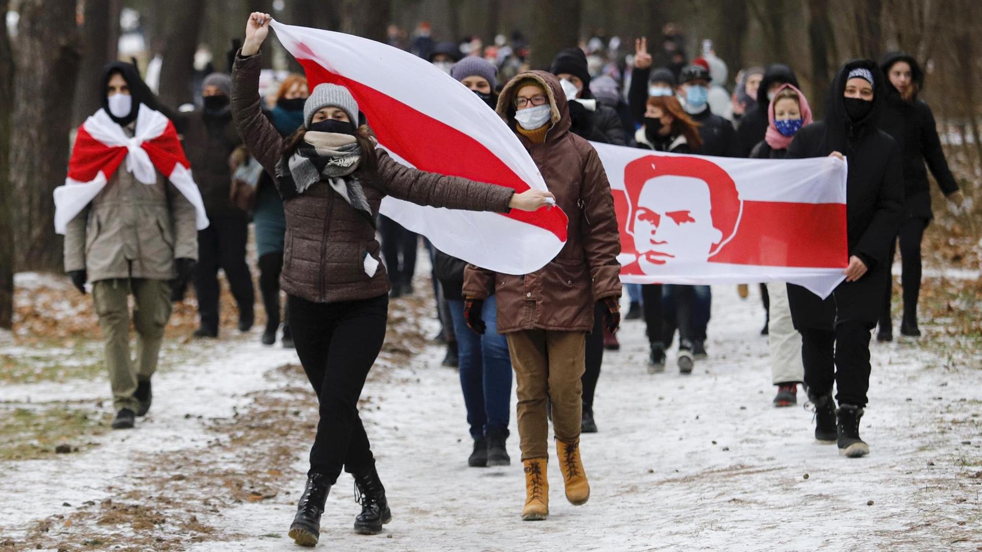 Demonstration gegen den belarusischen Präsidenten Lukaschenko im Dezember. Die Demonstrierenden laufen durch eine verschneite Landschaft, sie tragen die alte weiß-rot-weiße belarusische Flagge und wegen Corona Masken. Demonstration gegen den belarusischen Präsidenten Lukaschenko im Dezember. Die Demonstrierenden laufen durch eine verschneite Landschaft, sie tragen die alte weiß-rot-weiße belarusische Flagge und wegen Corona Masken.