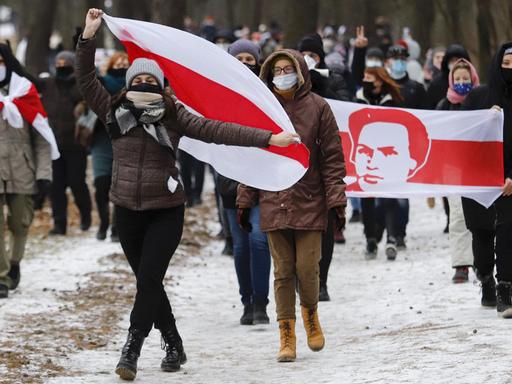 Demonstration gegen den belarusischen Präsidenten Lukaschenko im Dezember. Die Demonstrierenden laufen durch eine verschneite Landschaft, sie tragen die alte weiß-rot-weiße belarusische Flagge und wegen Corona Masken.