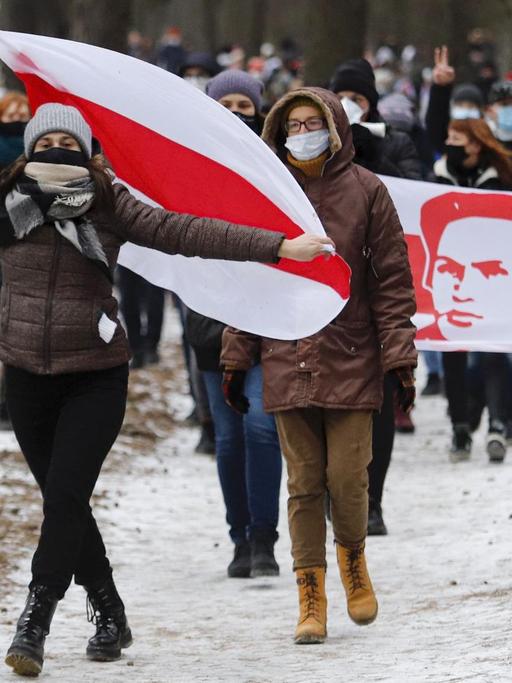 Demonstration gegen den belarusischen Präsidenten Lukaschenko im Dezember. Die Demonstrierenden laufen durch eine verschneite Landschaft, sie tragen die alte weiß-rot-weiße belarusische Flagge und wegen Corona Masken.