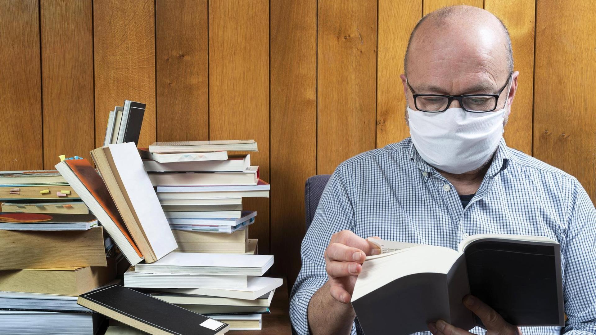 Ein Mann liest mit Gesichtsmaske ein Buch.