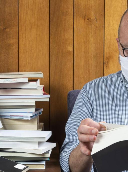Ein Mann liest mit Gesichtsmaske ein Buch.