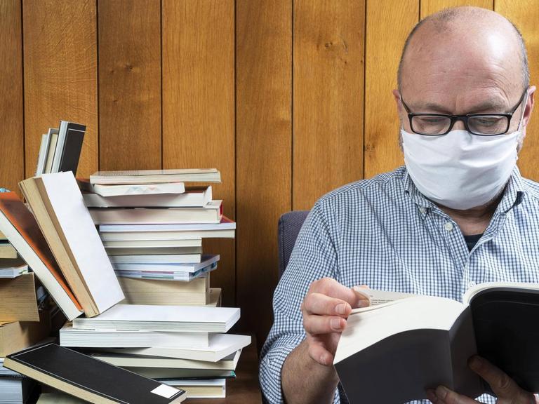 Ein Mann liest mit Gesichtsmaske ein Buch.