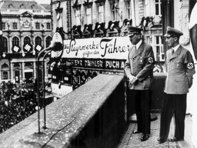 Der Führer und Reichskanzler Adolf Hitler (l) schaut mit Propagandaminister Dr. Joseph Goebbels am 14. März 1938, einen Tag nach dem Einmarsch der deutschen Wehrmacht in Österreich, vom Balkon des Hotels Imperial in Wien am Schwarzenbergplatz auf die ihm zujubelnde Menge, die sich vor dem Hotel versammelt hat.