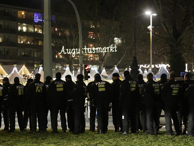 Polizisten stehen am 21.12.2015 in Dresden (Sachsen) am Rande einer Kundgebung des Bündnisses Pegida (Patriotische Europäer gegen die Islamisierung des Abendlandes) an einer Straße, während im Hintergrund der sogenannte Augustusmarkt zu sehen ist.