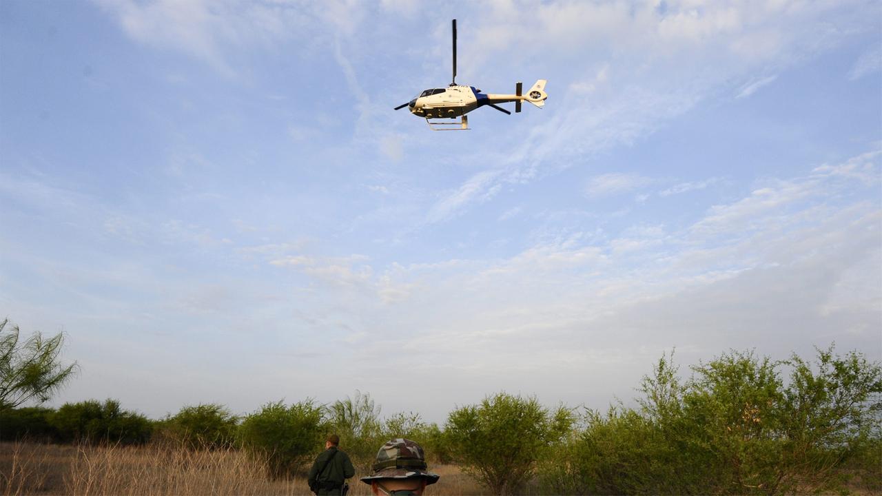 US-Grenzpolizisten patrouillieren auf einem Feld. Über ihnen sucht ein Hubschrauber nach Menschen, die den Fluss Rio Grande passieren wollen, um in die USA zu gelangen.