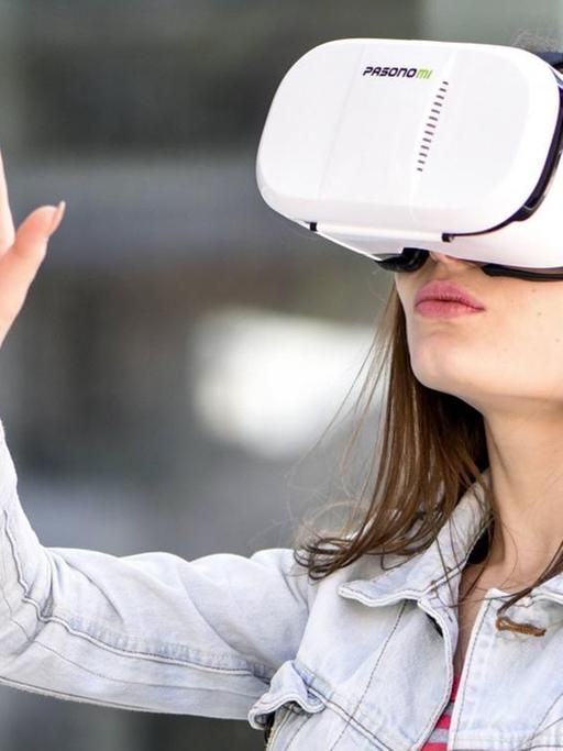 Junge Frau mit VR-Brille zeigt mit dem Finger in die Luft.
