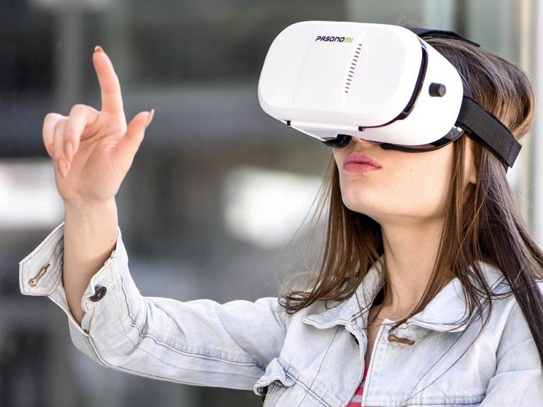 Junge Frau mit VR-Brille zeigt mit dem Finger in die Luft.