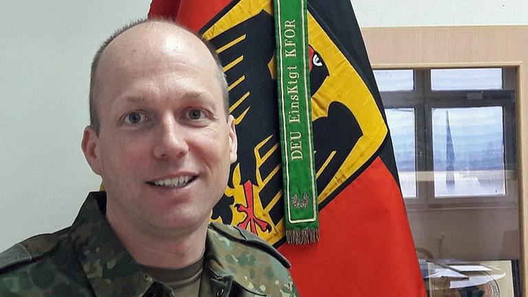 Oberstleutnant Christian Kiesel sitzt in Uniform vor einer Deutschlandfahne Oberstleutnant Christian Kiesel sitzt in Uniform vor einer Deutschlandfahne