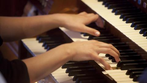 Zwei Hände bespielen das die mittlere Tastatur einer dreimanualigen Orgel.