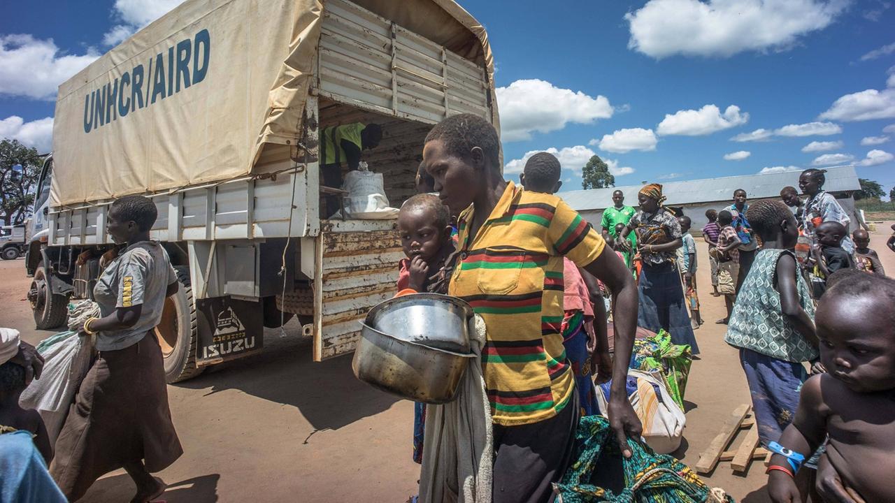 Mehrere Frauen mit Kindern gehen mit Bündeln und Geschirr im Arm über einen Platz. Mehrere Frauen mit Kindern gehen mit Bündeln und Geschirr im Arm über einen Platz.