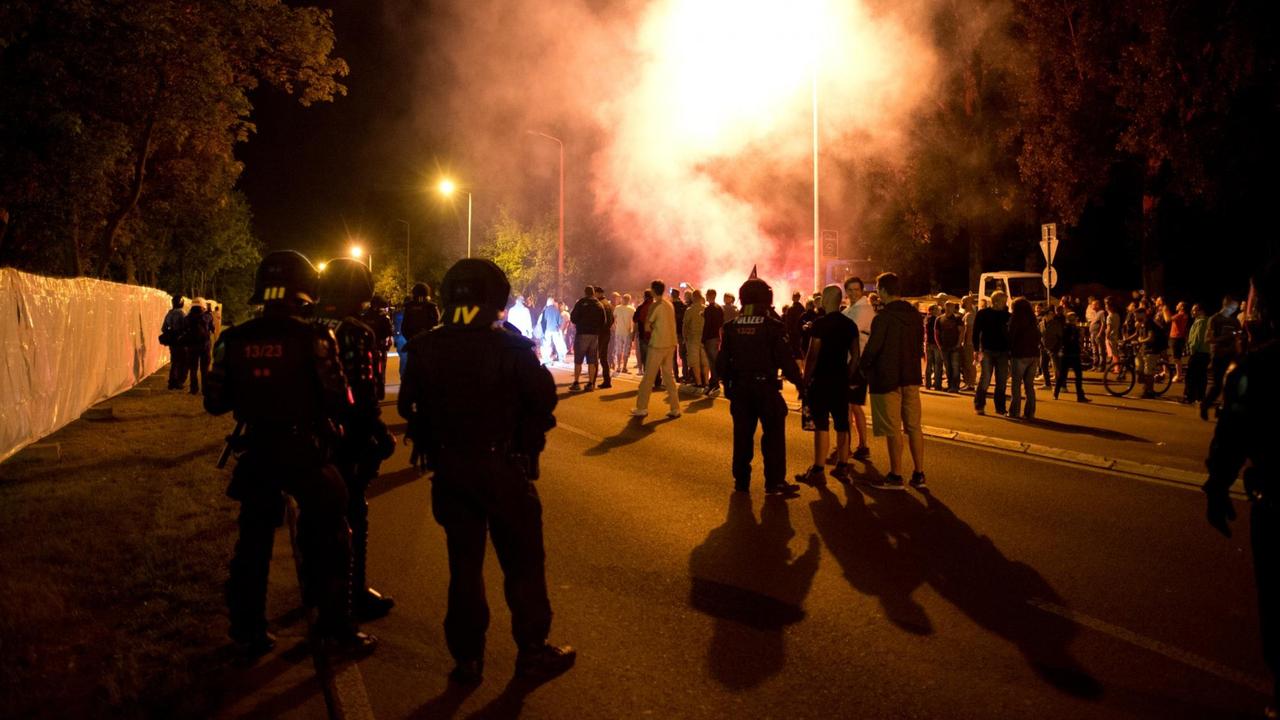 Demonstranten und Polizisten in Schutzkleidung.stehen in der Nacht auf einer Straße. Im Hintergrund sind Leuchtfeuer und Rauch zu sehen. Demonstranten und Polizisten in Schutzkleidung.stehen in der Nacht auf einer Straße. Im Hintergrund sind Leuchtfeuer und Rauch zu sehen.