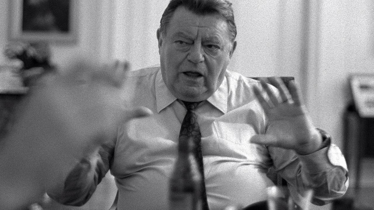 Schwarz-Weiß-Bild des damaligen bayerischen Ministerpräsidenten und CSU-Politikers Franz Josef Strauß: Er sitzt in einem weißen Hemd und Krawatte an einem Tisch und gestikuliert mit den Händen, im Vordergrund eine Bierflasche und Gläser. Schwarz-Weiß-Bild des damaligen bayerischen Ministerpräsidenten und CSU-Politikers Franz Josef Strauß: Er sitzt in einem weißen Hemd und Krawatte an einem Tisch und gestikuliert mit den Händen, im Vordergrund eine Bierflasche und Gläser.