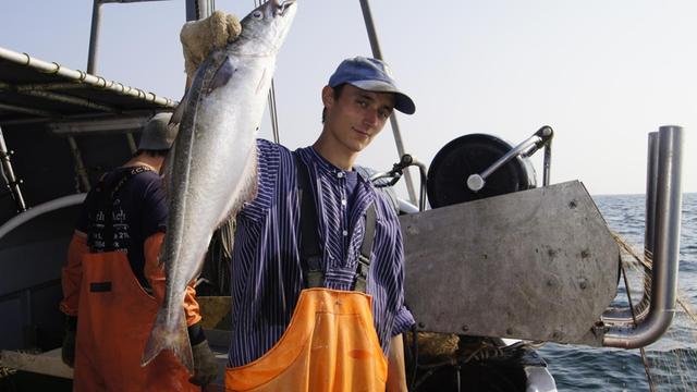 Der 22-jährige Ostseefischer Dennis Freita auf seinem Boot und mit einem Fisch in der rechten Hand.