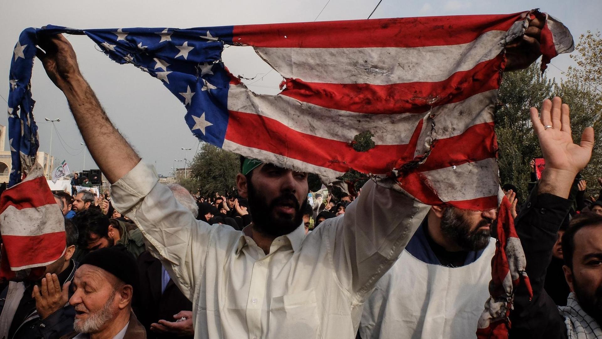 Während einer Anti-USA-Demonstration im Iran hält ein Teilnehmer eine zerrissene US-Flagge hoch.