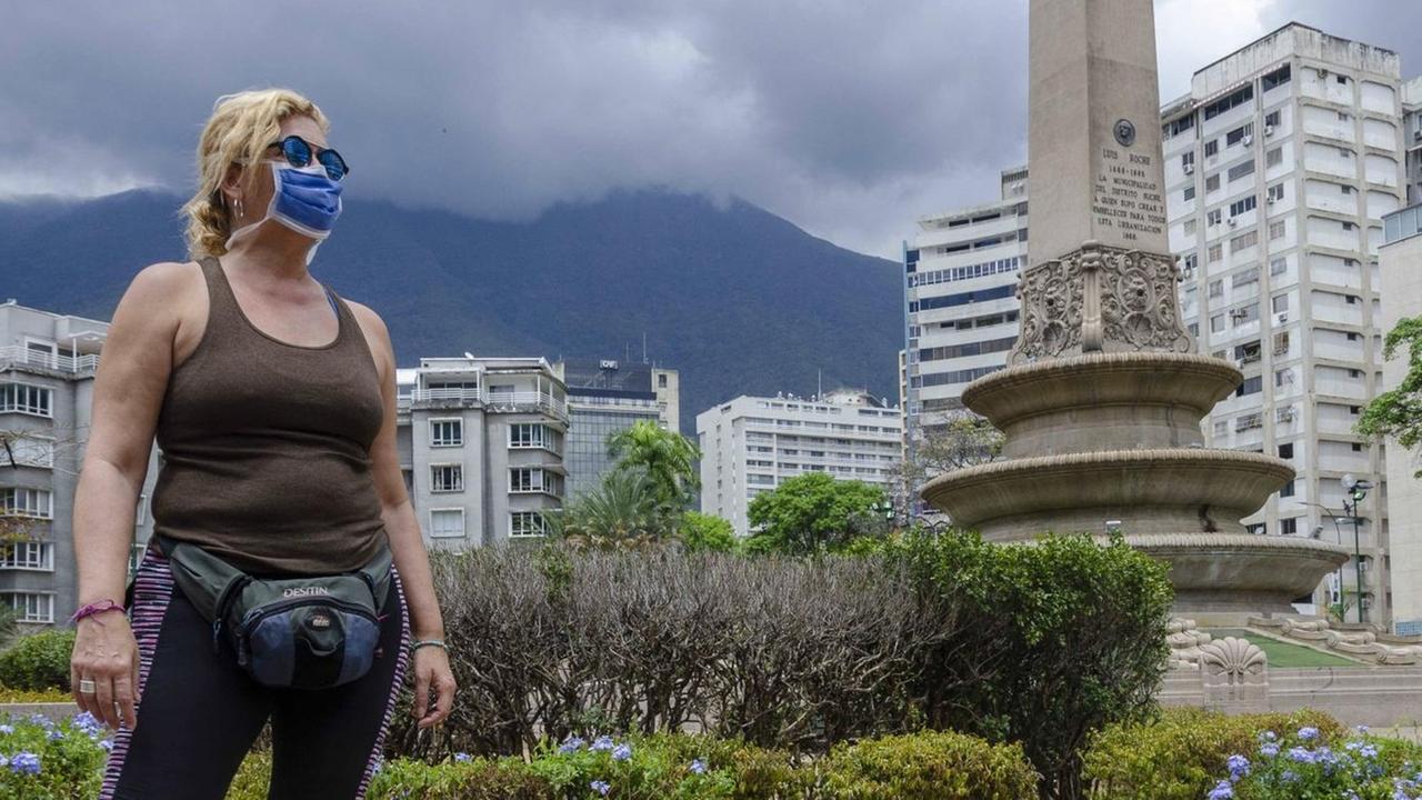 Eine Frau mit Schutzmaske steht trotzig auf einem Platz in Caracas. Eine Frau mit Schutzmaske steht trotzig auf einem Platz in Caracas.