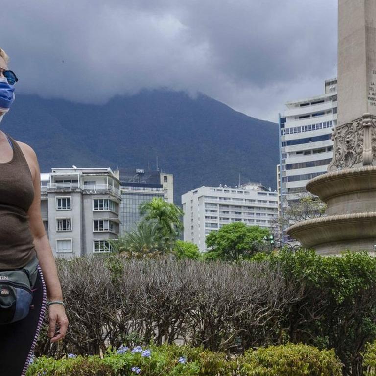 Eine Frau mit Schutzmaske steht trotzig auf einem Platz in Caracas.