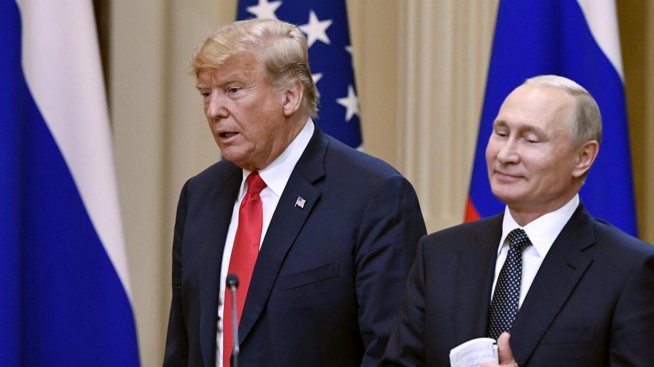 Trump sagt etwas, Putin steht lächelnd daneben. Vor ihnen ein Schild mit der Aufschrift "Helsinki 2018", hinter ihnen die Fahnen beider Staaten. Trump sagt etwas, Putin steht lächelnd daneben. Vor ihnen ein Schild mit der Aufschrift "Helsinki 2018", hinter ihnen die Fahnen beider Staaten.